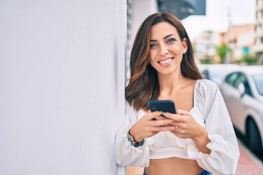 Genç İspanyol kadın şehirde akıllı telefon kullanarak mutlu bir şekilde gülümsüyor..