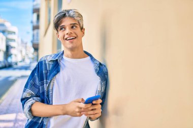 Genç İspanyol adam şehirde akıllı telefon kullanarak mutlu gülümsüyor..