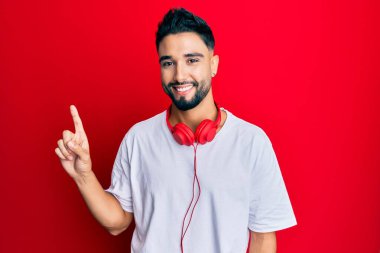 Sakallı genç adam kulaklıkla müzik dinleyip başarılı bir fikir işaret ediyor. Heyecanlı ve mutlu. Bir numara.. 