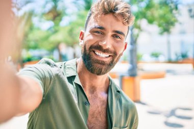 Genç İspanyol gülümseyen adam parkta fotoğraf çekerken mutlu oluyor.