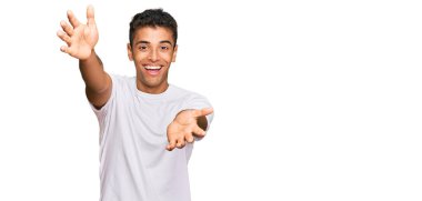 Genç, yakışıklı, Afro-Amerikan bir adam, günlük beyaz tişörtler giyip kameraya bakıyor. Sarılmak için kollarını açmış gülümsüyor. Mutluluğu kucaklayan neşeli bir ifade.. 