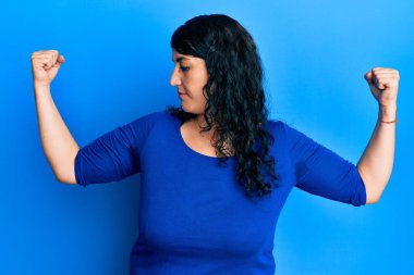 Artı mavi gömlekli esmer kadın gururla gülümseyen kol kaslarını gösteriyor. fitness konsepti. 