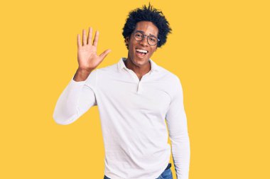 Afro saçlı, sıradan giyinmiş ve gözlüklü yakışıklı Afro-Amerikalı adam merhaba diyor mutlu ve gülümsüyor, dostça karşılama jesti. 