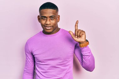 Gündelik pembe süveter giyen genç siyahi adam başarılı bir fikri işaret ediyor. Heyecanlı ve mutlu. Bir numara.. 