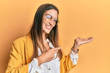 İş stili ve gözlük takan genç ve güzel bir kadın kameraya hayret ediyor ve gülümsüyor.. 