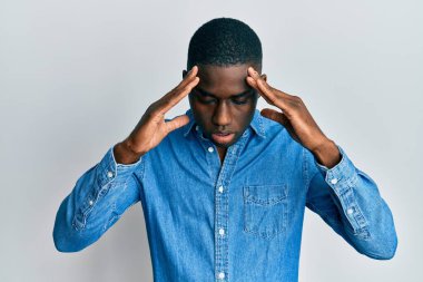 Genç, Afro-Amerikan bir adam, günlük kıyafetler giyiyor, eli başının üstünde, stres yüzünden başı ağrıyor. migren ağrısı. 