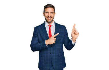 Sakallı, takım elbiseli, kravatlı, gülümseyen ve kameraya bakan yakışıklı bir adam.. 