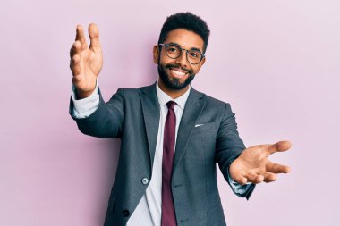 Sakallı, takım elbiseli ve kravatlı yakışıklı, kucaklaşmak için kollarını açıp kameraya gülümseyen bir iş adamı. Mutluluğu kucaklayan neşeli bir ifade.. 
