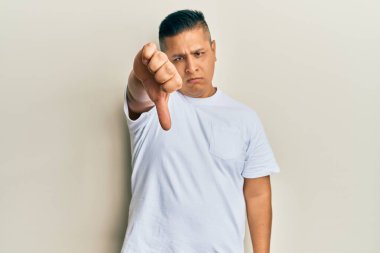 Gündelik beyaz tişört giyen genç latin adam mutsuz ve kızgın görünüyor. Reddedilmiş ve olumsuz jestler yapıyor. kötü ifade. 