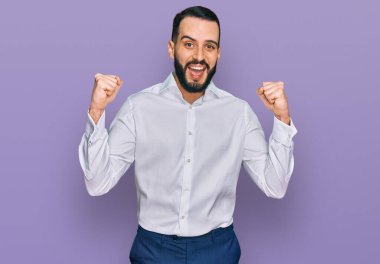 Sakallı, iş gömleği giyen genç adam şaşırmış ve şaşırmış bir şekilde kolları açık ve gözleri açık bir şekilde başarıyı kutluyor. Kazanan konsept. 