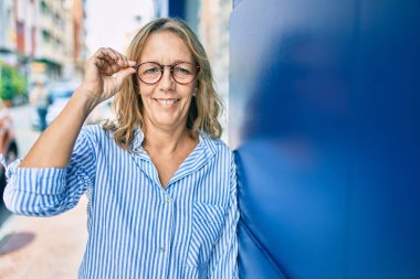 Orta yaşlı, beyaz bir kadın şehirde mutlu bir şekilde dikiliyor..