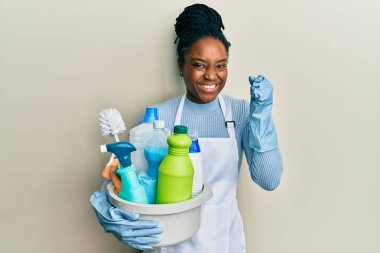 Saçları örgülü, önlüklü, temizlik ürünleri taşıyan Afrikalı Amerikalı bir kadın gururla bağırıyor, zaferi ve başarıyı kutluyor ve kollarını kaldırarak heyecanlanıyor. 