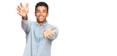 Genç, yakışıklı, Afro-Amerikan bir adam günlük giysiler içinde kameraya bakıyor ve sarılmak için kollarını açmış gülümsüyor. Mutluluğu kucaklayan neşeli bir ifade.. 