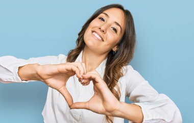 Genç esmer kadın, gündelik giysiler giyip, aşıkken gülümsüyor, elleriyle kalp sembolü yapıyor. romantik kavram. 