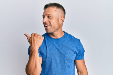 Yakışıklı, kaslı, günlük kıyafetler giyen, baş parmağını kaldıran, ağzı açık gülümseyen bir adam. 