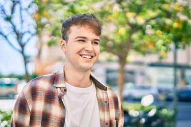 Genç beyaz adam gülümseyerek şehirde mutlu mesut duruyor..