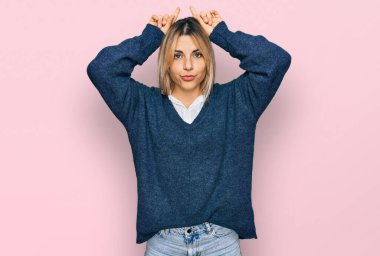 Kafkasyalı genç bir kadın, günlük kıyafetler giyip parmaklarını boynuzlarına geçirip komik jestler yapıyor. 