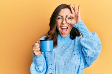 Genç esmer kadın elinde bir fincan kahveyle gülümsüyor. Mutluluktan gülümsüyor. 