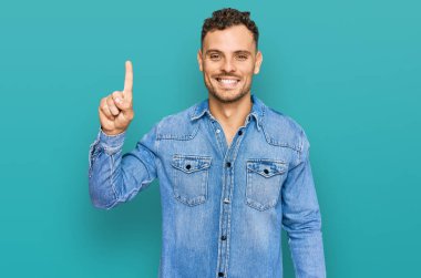 Günlük kot ceket giyen genç İspanyol bir numarayı gösterip işaret ederken kendinden emin ve mutlu bir şekilde gülümsüyor.. 