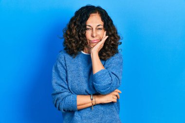 Orta yaşlı İspanyol bir kadın günlük kıyafetler giyip kollarını kavuşturarak depresyondan sıkılmış ve yorgun görünüyor.. 