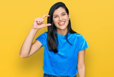 Gündelik kıyafetler giyen, gülümseyen, kendine güvenen, el hareketi yapan, parmaklarıyla işaret yapan ve kameraya bakan genç İspanyol kadın. ölçüm kavramı. 