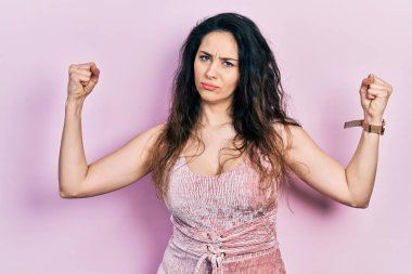 Sıradan kıyafetler giyen genç İspanyol kadın gururla gülümseyen kol kaslarını gösteriyor. fitness konsepti. 