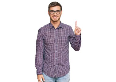 Yakışıklı, beyaz, günlük kıyafetler ve gözlük takan bir numaralı parmağını gösterip onu işaret eden kendine güvenen ve mutlu bir adam.. 