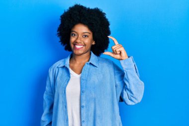 Genç Afro-Amerikalı kadın, günlük kıyafetler giymiş, gülümseyen ve el hareketleriyle küçük boy işaretler yapan, parmaklarıyla işaret eden ve kameraya bakan. ölçüm kavramı. 