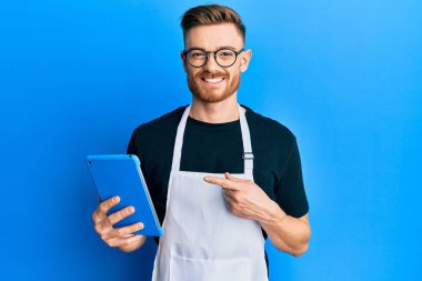 Genç kızıl saçlı adam profesyonel önlük giyiyor dokunmatik ped kullanıyor mutlu bir şekilde parmakla işaret ediyor. 