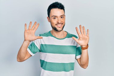 Gündelik kıyafetler giyen genç İspanyol adam on numarayı gösterip işaret ederken kendinden emin ve mutlu bir şekilde gülümsüyor.. 