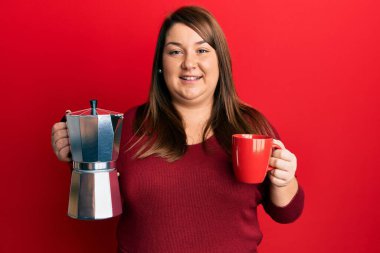 Güzel esmer, iri yarı, İtalyan kahvesi içen mutlu ve havalı bir gülümsemeyle gülümseyen bir kadın. diş gösterme. 