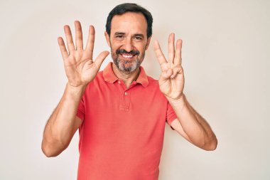 Orta yaşlı İspanyol bir adam gündelik kıyafetler giyer ve 8 numaralı parmaklarıyla gülümseyerek mutlu ve kendinden emin bir şekilde işaret eder.. 