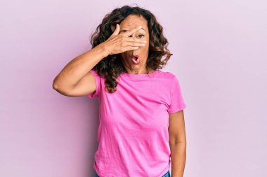 Orta yaşlı İspanyol kadın gündelik giysiler giymiş. Şoka girmiş. Yüzü ve gözlerini kapamış, utanmış ifadesiyle parmaklarından bakıyor.. 