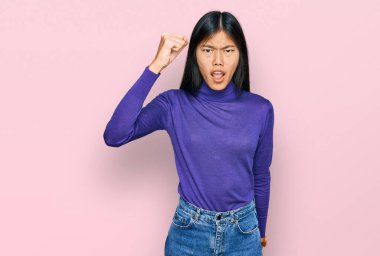 Güzel, genç Asyalı bir kadın, gündelik giysiler giymiş kızgın ve kızgın yumruğunu kaldırırken öfkeyle bağırıyor. öfke ve agresif konsept. 