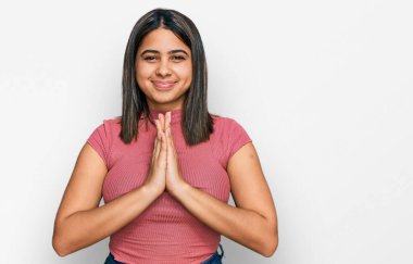 Gündelik tişört giyen genç İspanyol kız elleri birarada dua ediyor af diliyor kendinden emin bir şekilde gülümsüyor.. 