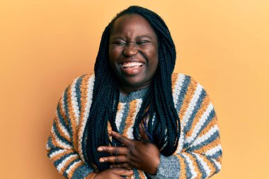 Saçları örgülü genç siyah bir kadın, sıradan bir kazak giyiyor, gülümsüyor ve kahkahalar atıyor.. 