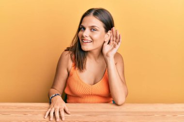 Gündelik giysiler giymiş genç beyaz bir kadın masaya oturmuş, sırıtarak dedikodu ve dedikoduları dinliyor. Sağırlık kavramı. 