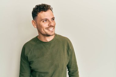 Gündelik kıyafetler giyen genç İspanyol bir adam yüzünde gülümsemeyle yan yana bakıyor, doğal bir ifade. Kendinden emin gülen. 