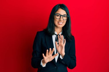 Güzel Asyalı genç kadın iş elbisesi giymiş tiksindirici bir ifade, tiksinti dolu ve tiksindirici bir yüz ifadesi takınıyor. Eller havada. 