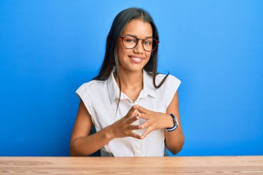 Masada el pençe divan oturan, rahat ve neşeli gülümseyen Latin kökenli güzel bir kadın. Başarı ve iyimserlik 