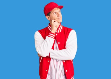 Beyzbol üniforması giyen yakışıklı bir adam ciddi bir yüz ifadesi var. Elleri çenesinde soru sormayı düşünüyor. Kafa karıştırıcı bir fikir. 