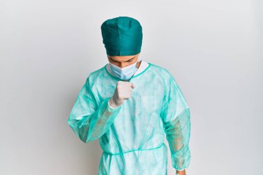Cerrah üniforması ve tıbbi maske takan yakışıklı genç adam kendini iyi hissetmiyor ve soğuk algınlığı veya bronşitin belirtisi olarak öksürüyor. sağlık hizmeti kavramı. 