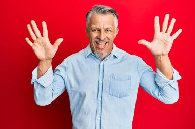 Orta yaşlı, gri saçlı, günlük kıyafetler giyen, on numaralı parmaklarıyla işaret eden, kendinden emin ve mutlu bir adam.. 