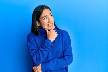 Sıradan bir kazak giyen genç Asyalı kadın bir soru hakkında endişeli ve gergin bir şekilde düşünüyor. 