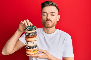 Genç kızıl saçlı adam elinde lezzetli renkli çöreklerle kameraya bakıyor. Öpüşme sahnesi çekiliyor ve çok seksi. aşk ifadesi. 