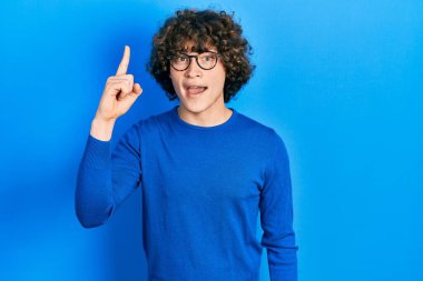 Gündelik kıyafetler giyen ve gözlük takan yakışıklı genç adam başarılı bir fikirle işaret ediyor. Heyecanlı ve mutlu. Bir numara.. 