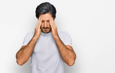 Genç İspanyol bir adam, stresten dolayı başı ağrıyan günlük beyaz tişörtler giyiyor. migren ağrısı. 