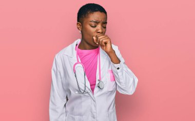 Doktor üniforması ve steteskop giyen genç Afro-Amerikan kadın kendini iyi hissetmiyor ve soğuk algınlığı veya bronşitin belirtisi olarak öksürüyor. sağlık hizmeti kavramı. 