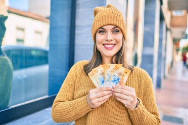Gülümseyen genç sarışın kadın şehirde İsviçre frangı banknotları tutuyor..