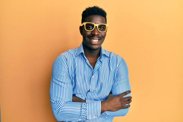 Handsome black man wearing yellow glasses happy face smiling with crossed arms looking at the camera. positive person.